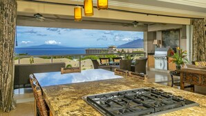 Una cocina moderna con estufa a gas, comedor con mobiliario de mimbre y vistas al océano.