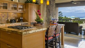 Una cocina con una isla grande, taburetes de bar y vista al océano.