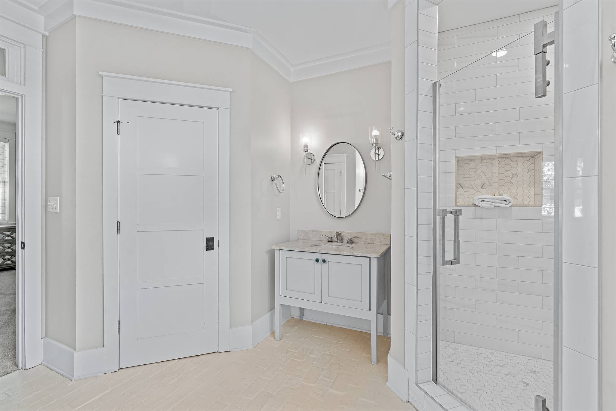A bathroom with a white vanity, a round mirror, and a glass-enclosed shower.