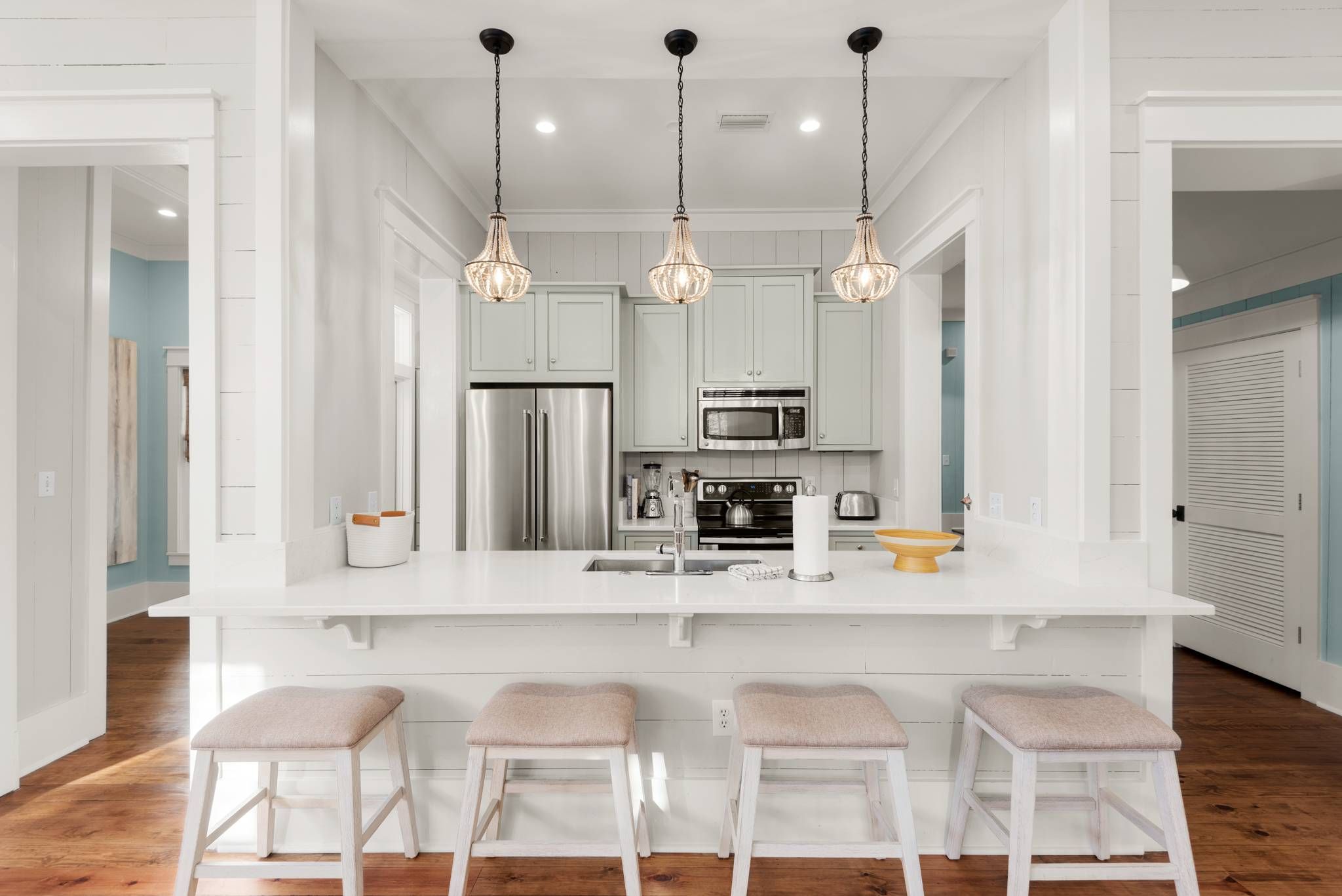 Une cuisine moderne avec des meubles blancs, des appareils en acier inoxydable et trois lampes suspendues.