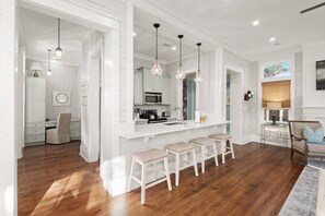 A modern kitchen with white cabinetry, a central island with stools, pendant lighting, and a view of the dining area.