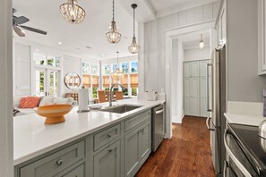 A modern kitchen with grey cabinets, a large island, stainless steel appliances, and pendant lighting.