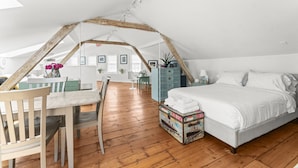 Une chambre spacieuse située sous les combles, avec un plafond en pente, un plancher en bois, un lit, un bureau et une commode.