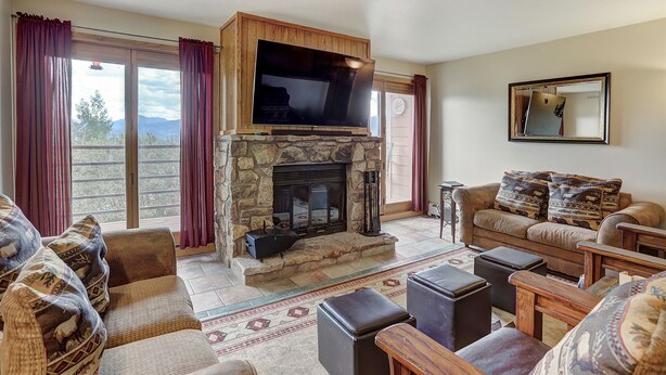 A living room with a stone fireplace, leather sofas, and a large flat-screen TV mounted above the fireplace. - Beautiful Condo, Sleeps 8, Gorgeous Views, Wood Fireplace, HDTV, Hot Tubs - BB (Silverthorne)