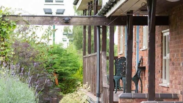 Ein gepflasterter Weg führt zu einem Backsteinhaus mit einer Holzveranda und einem grünen Stuhl.