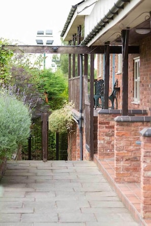 A stone pathway leading to a brick building with a wooden porch and a green chair. - The Hanmer Arms (Whitchurch)