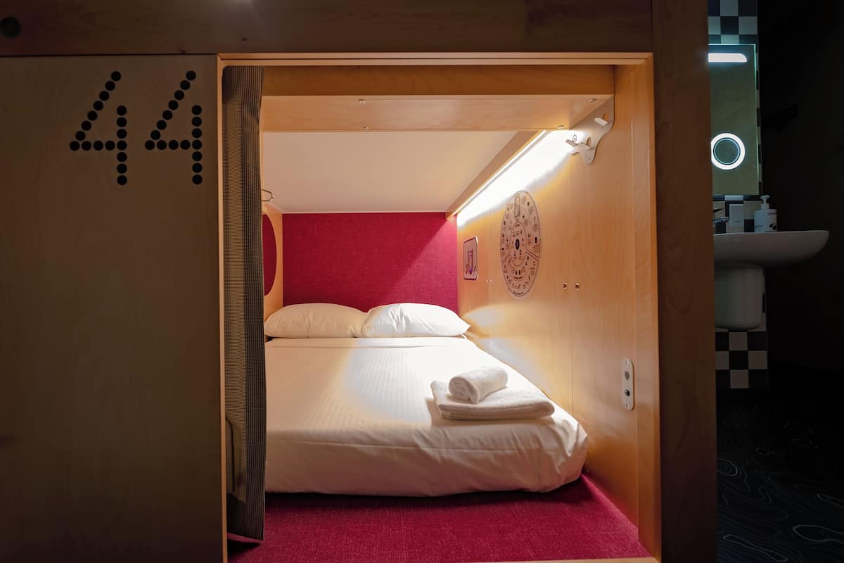 A compact room with a bed, a red carpet, a wooden door with the number 44, and a small bathroom with a sink and mirror.
