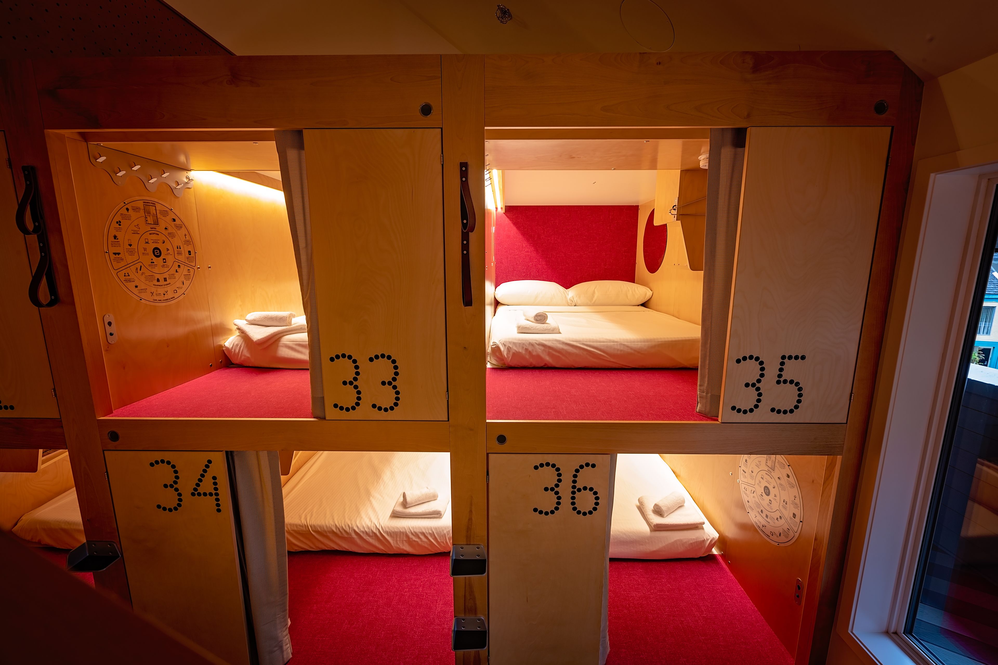 Four wooden bunk beds with numbers 33, 34, 35, and 36, each with a red carpet and white bedding.