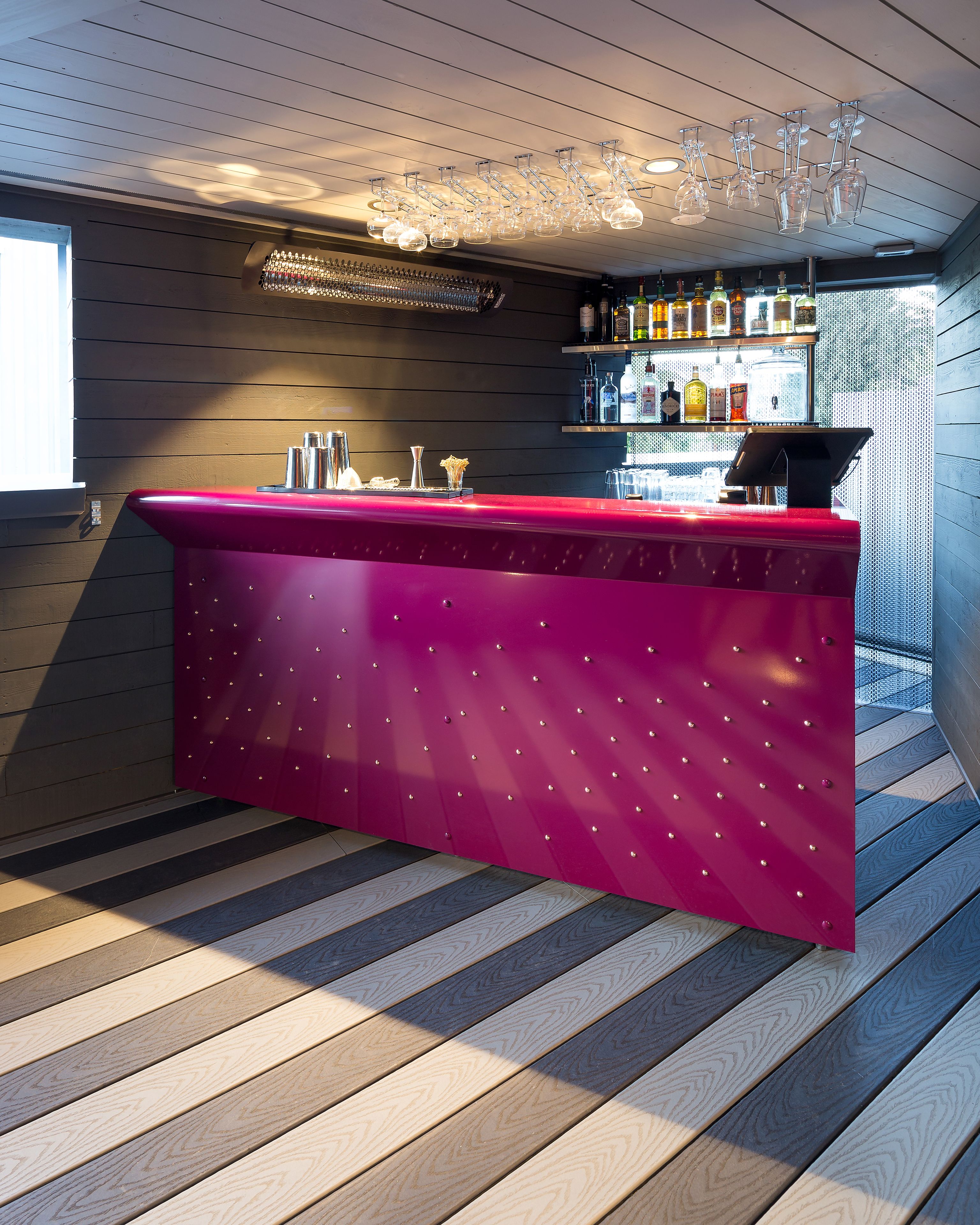 A bar area with a red counter, wooden flooring, and a ceiling with hanging glassware.