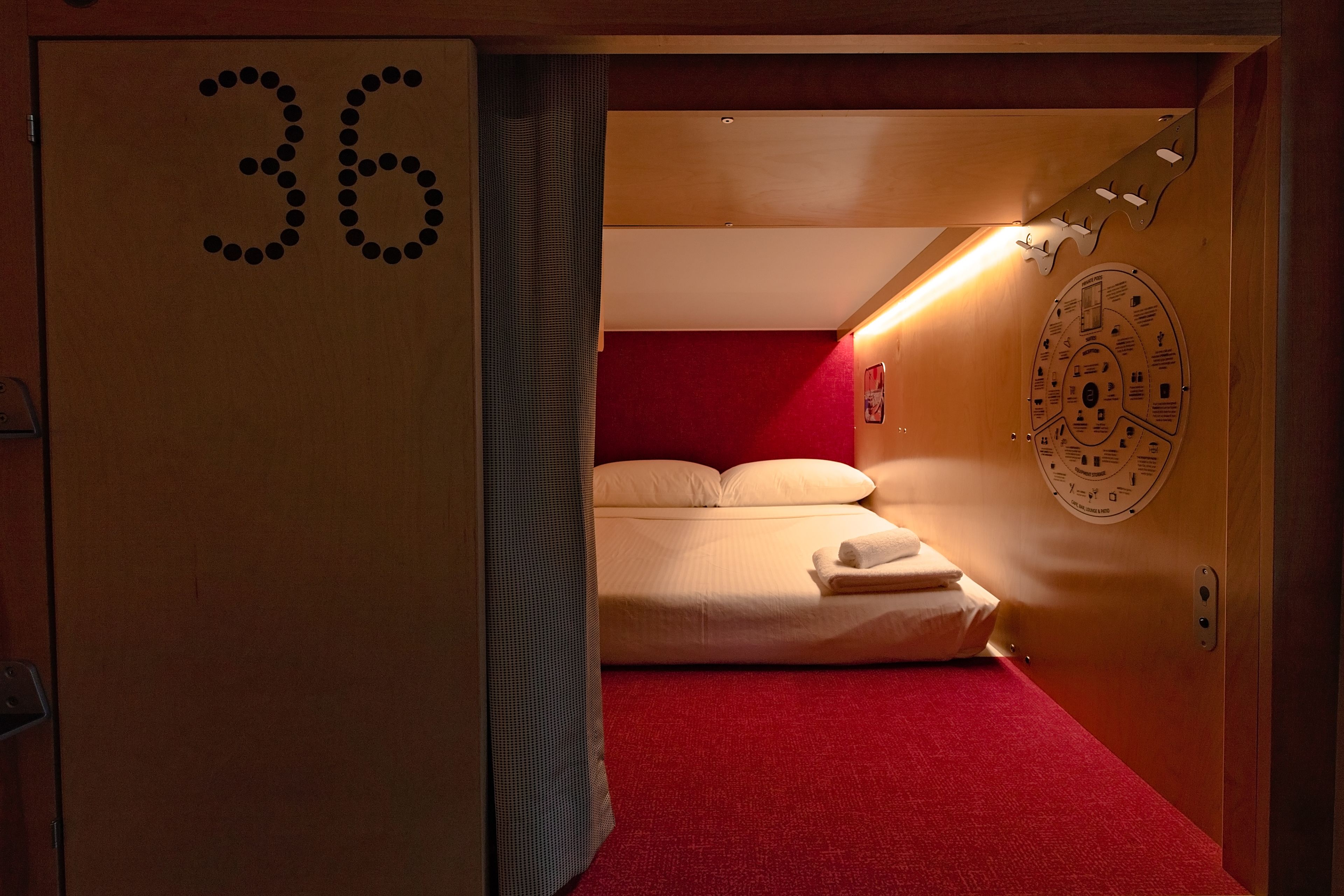 A hotel room with a red carpet, a bed with white linens, a wooden door with the number 36, and a wall clock.