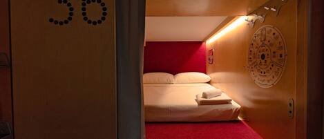 A hotel room with a red carpet, a bed with white linens, a wooden door with the number 36, and a wall clock.