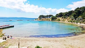 A beach with clear water, a boat docked on the left, and people relaxing on the sand. - Beach House Split (Split)