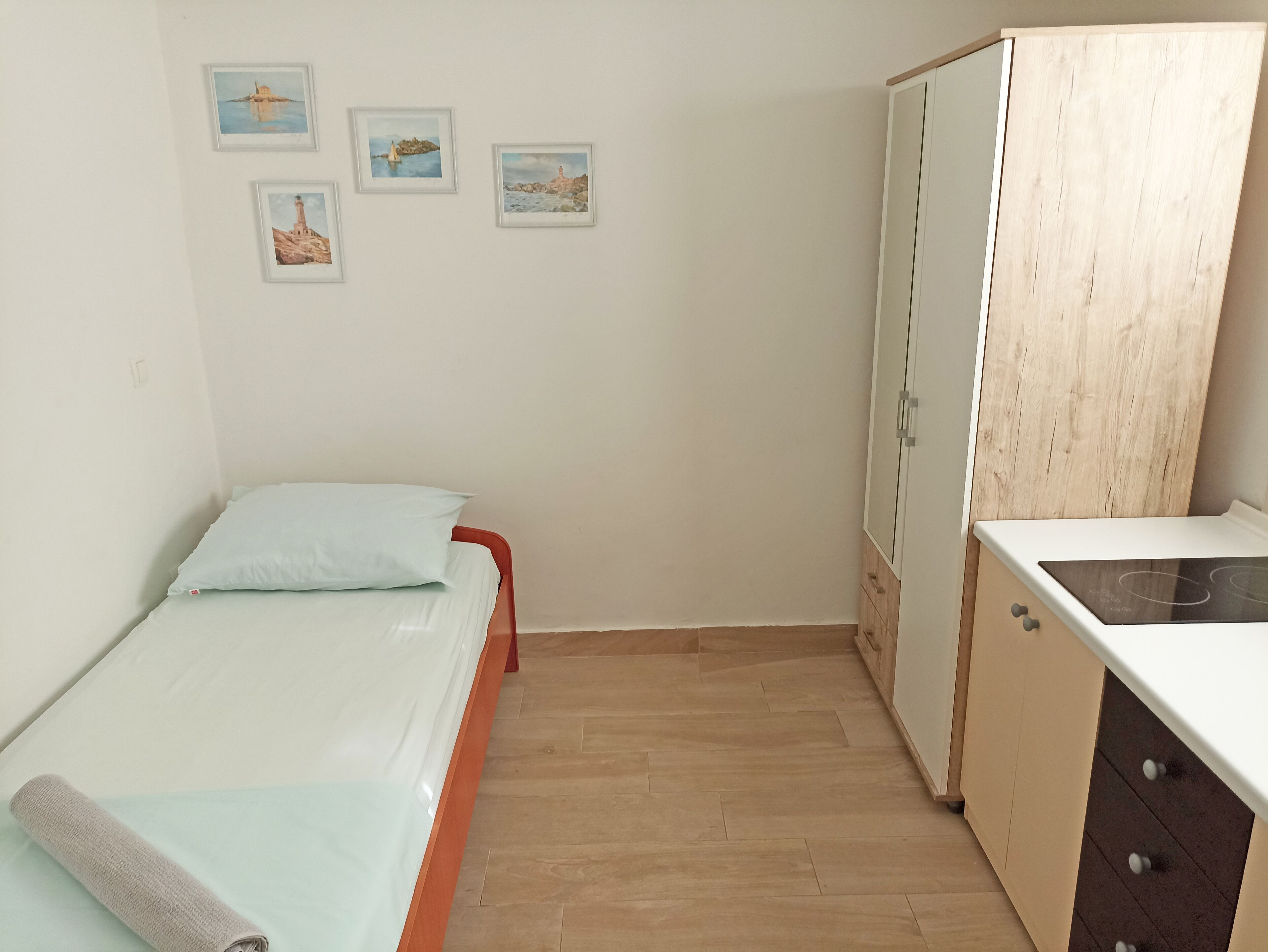 Une petite pièce bien rangée, comprenant un lit, une armoire et un coin cuisine.