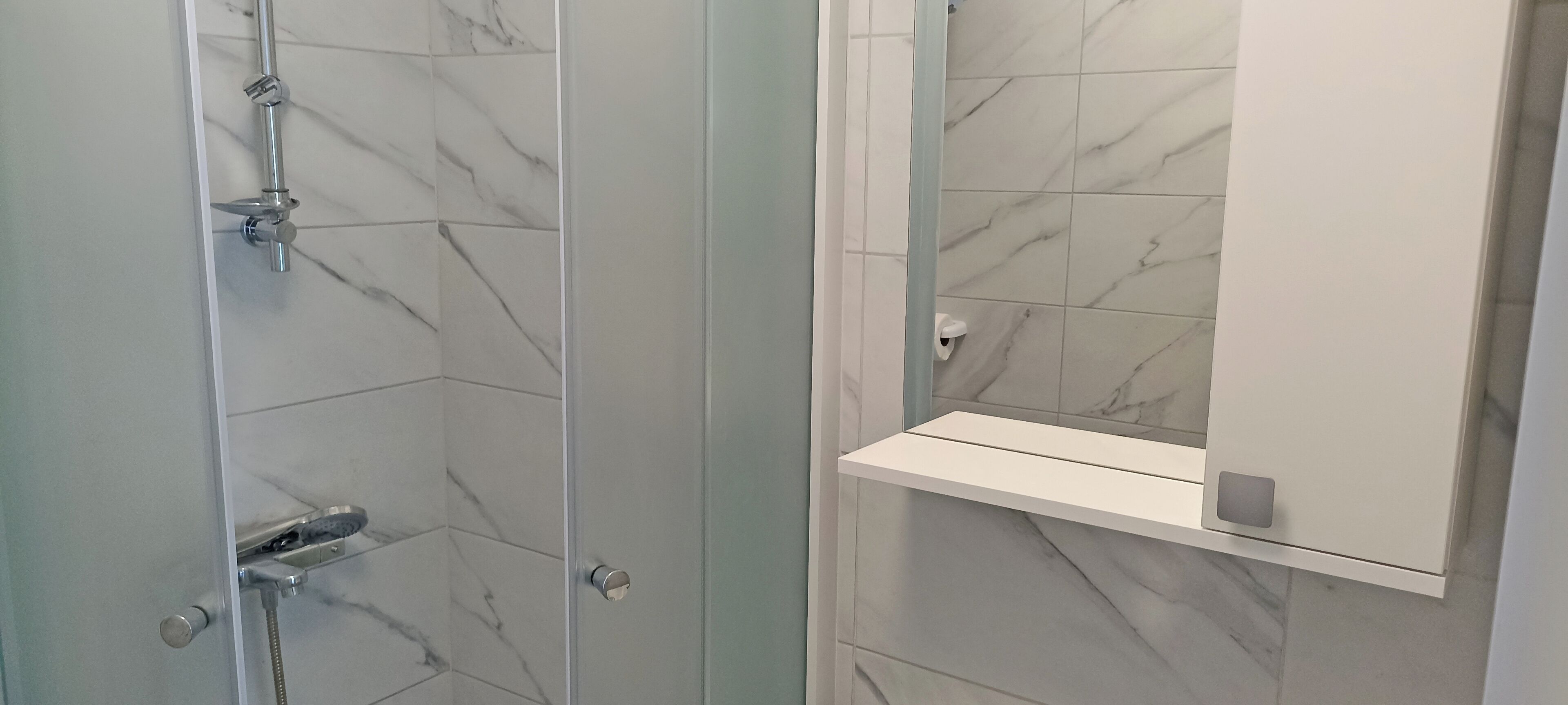 A bathroom with a shower, a mirror, and a shelf.