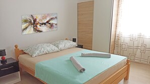 A neatly made bed with a light blue bedspread and two pillows, a wooden headboard, a bedside table with a lamp, and a wall-mounted abstract painting. - Beach House Split (Split)