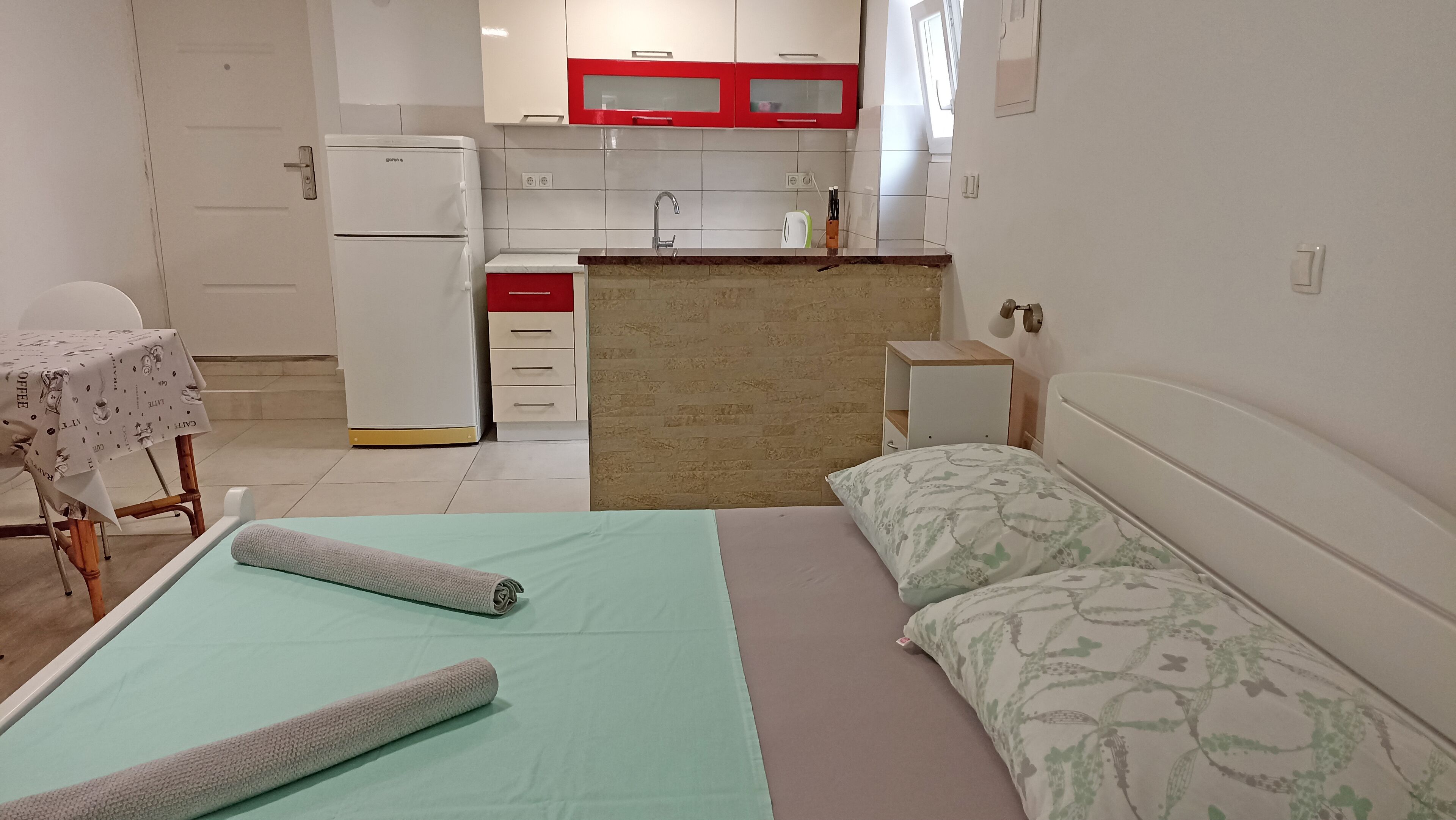 Een kleine hotelkamer met een bed, een kitchenette, een tafel met tafelkleed en een stoel.