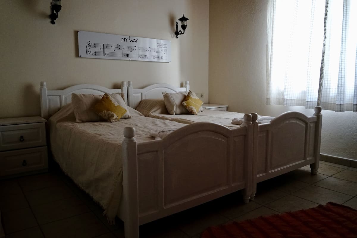 Een slaapkamer met een tweepersoonsbed, twee nachtkastjes, een wandlamp en een raam met gordijnen.
