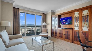 A hotel room with a large window, a flat-screen TV, a sofa, a chair, and a coffee table.
