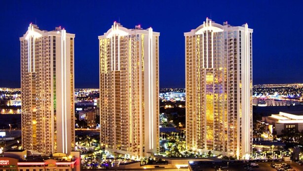 Three high-rise buildings with multiple floors, likely residential or hotel towers, with a cityscape in the background.