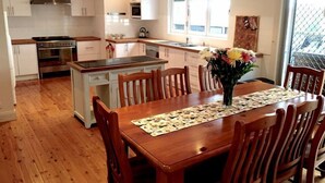 Une cuisine moderne avec des meubles blancs, un îlot central et un coin repas comprenant des chaises et une table en bois.