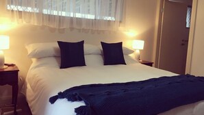 Un lit bien fait, avec du linge de lit blanc et deux oreillers foncés, une couverture bleue et deux lampes de chevet.