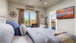 Ein Schlafzimmer mit einem großen Bett, einem Fenster mit Vorhängen, einer Wanduhr, einem Wand-Fernseher und Blick auf die Wüste.