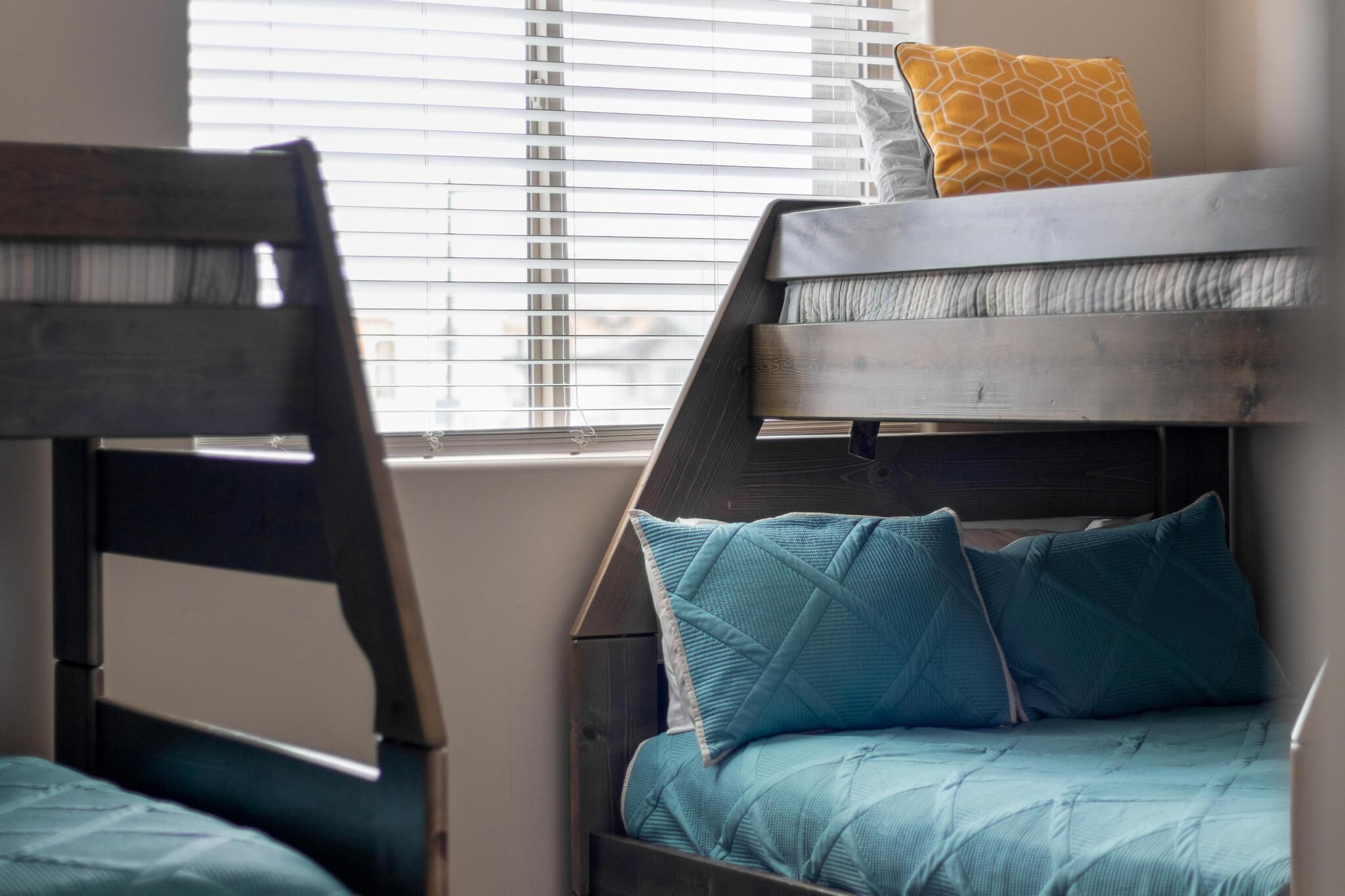 A bunk bed with a wooden headboard and a window with blinds in the background.
