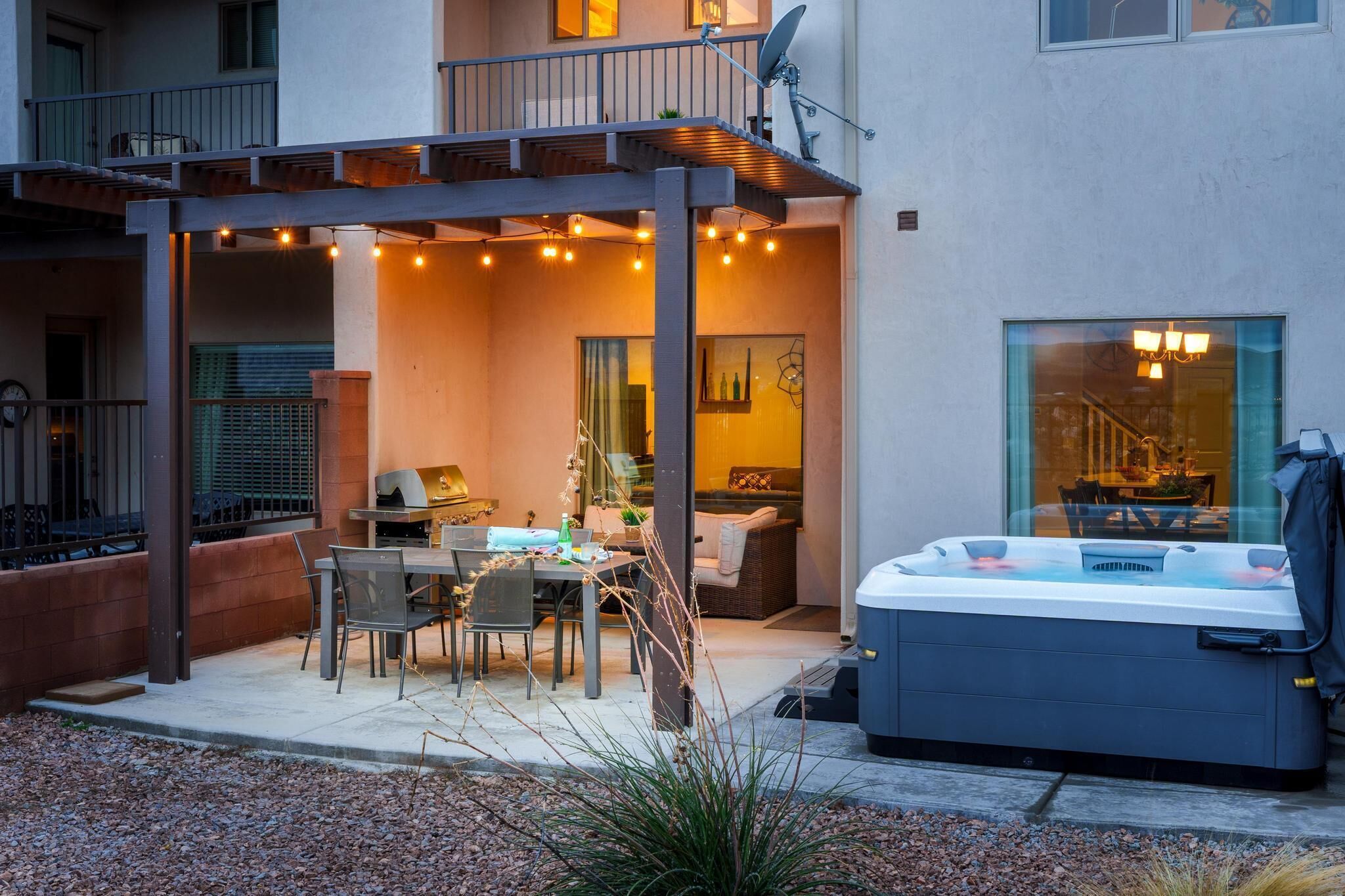 An outdoor patio with a hot tub, dining table, chairs, and string lights.