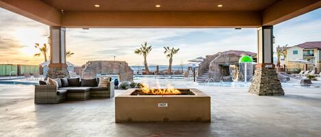 A covered outdoor area with a fire pit labeled "HOT" and a seating area with a view of the pool and buildings in the background.