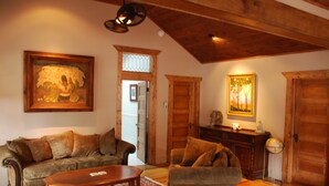 A cozy living room with a wooden ceiling, a sofa, a coffee table, and two paintings. - Historic Riverside Cottage ~ A Beautifully Restored 1908 Cottage! (Estes Park)