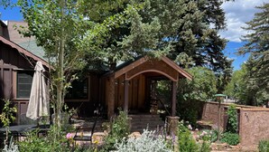 A rustic lodge with a stone facade, a wooden porch, and a garden with various plants and rocks. - Historic Riverside Cottage ~ A Beautifully Restored 1908 Cottage! (Estes Park)
