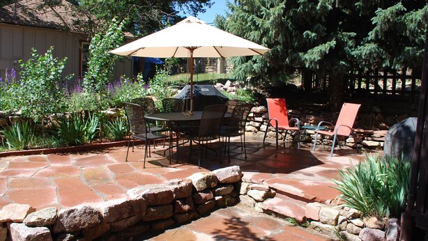 An outdoor patio with stone flooring, a table with chairs, and an umbrella. - Historic Riverside Cottage ~ A Beautifully Restored 1908 Cottage! (Estes Park)