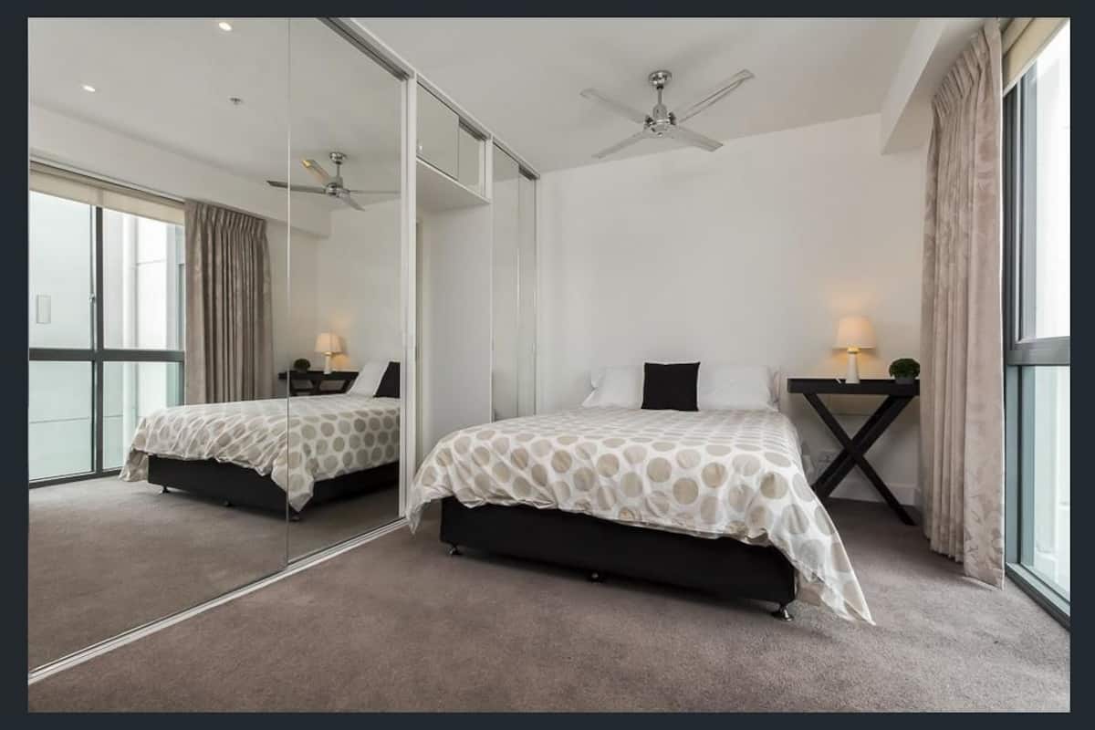 A modern bedroom with two beds, a large mirror, and a ceiling fan.