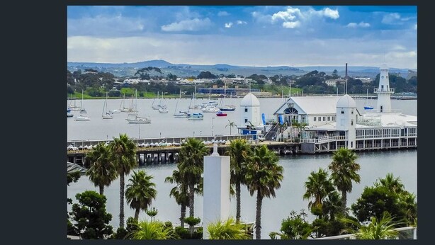 A marina with boats, a lighthouse, and a building with a dome and flag. - Waterfront By Gold Star Stays (Geelong)