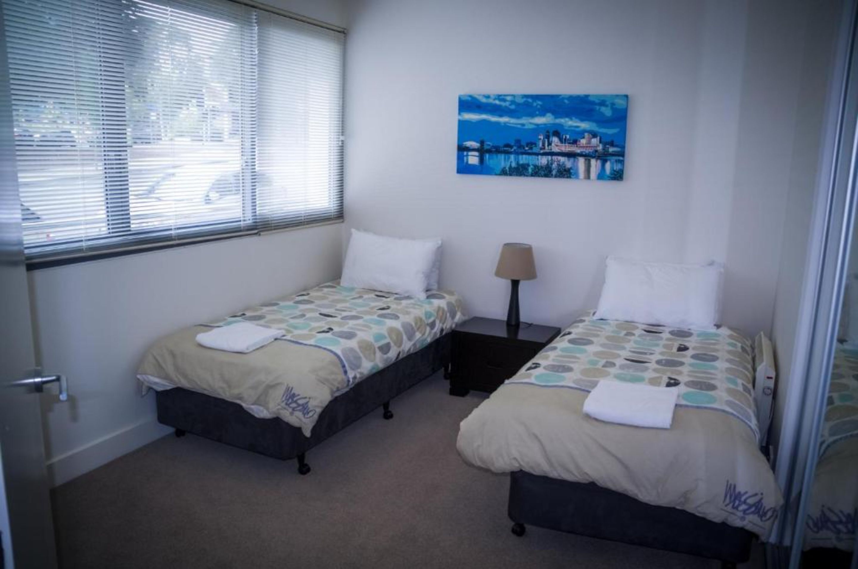 A room with two single beds, a nightstand, a lamp, and a painting on the wall.