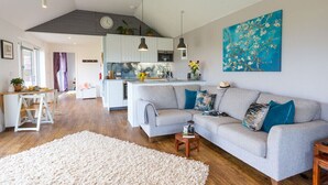 A modern living room with a grey sofa, a white rug, and a kitchen in the background. - Luxury what ever the weather (Wellington)