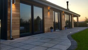 A modern building with large sliding glass doors, a covered patio area, and a well-maintained lawn. - Luxury what ever the weather (Wellington)