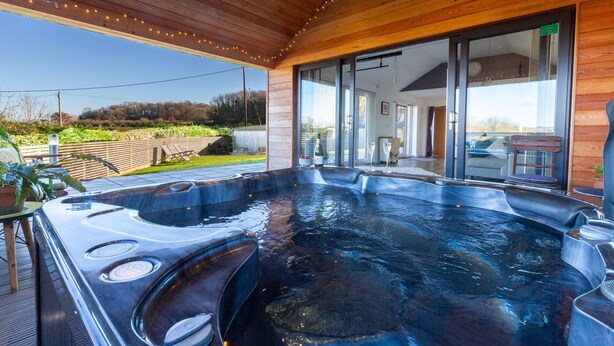 A hot tub with a wooden deck and a glass door leading to an indoor area. - Luxury what ever the weather (Wellington)