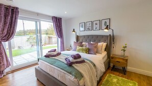A bedroom with a large bed, a nightstand, a lamp, and a view of the outdoors. - Luxury what ever the weather (Wellington)
