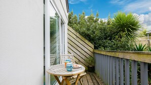 Een houten terras met een tafel en stoelen, een plant in een pot en uitzicht op groen.