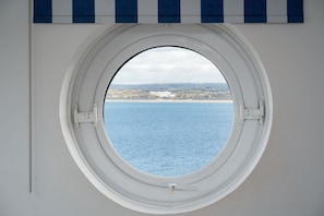 Una ventana redonda con vista al mar y un paisaje lejano.