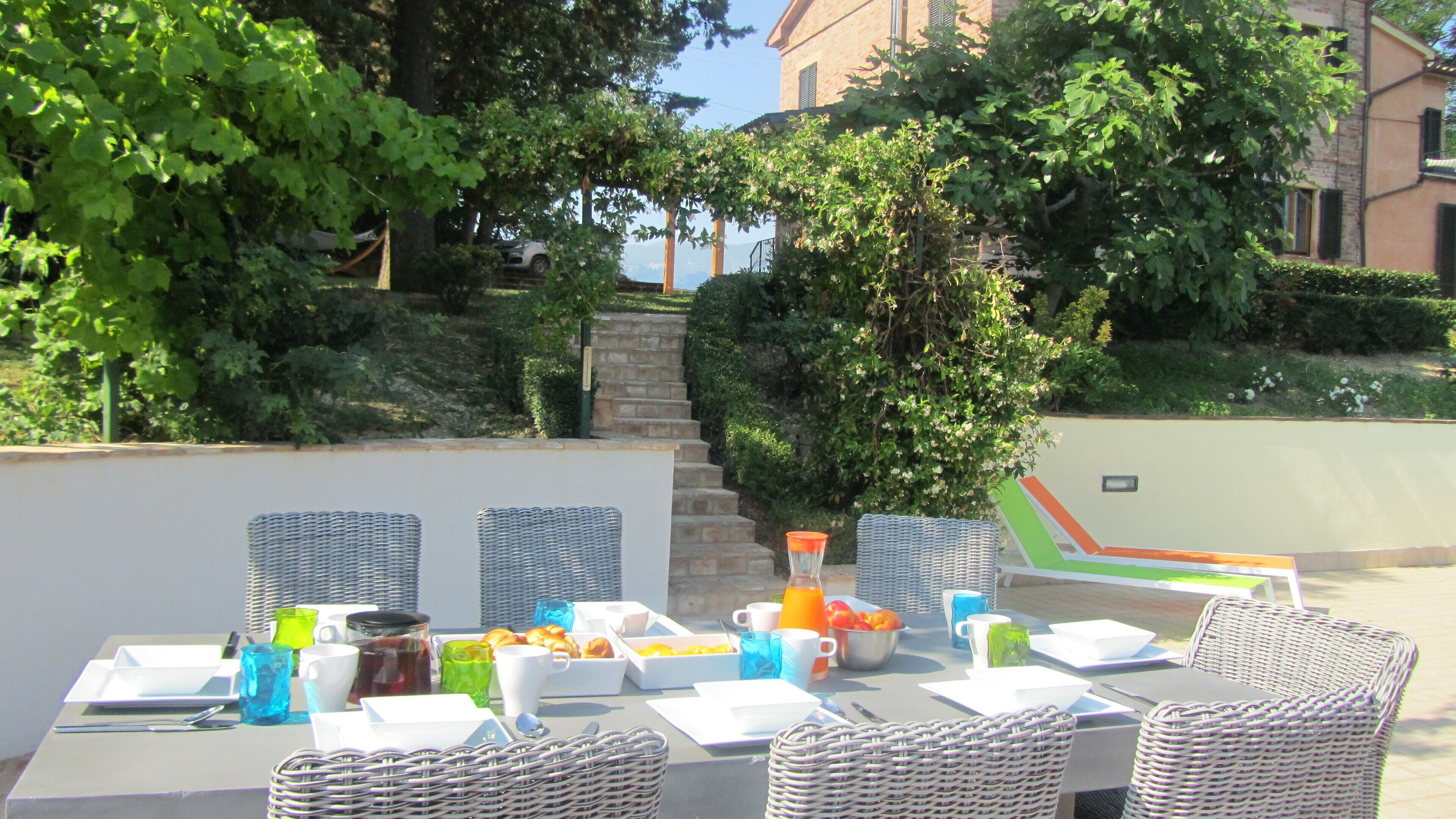 Un espace extérieur aménagé pour prendre les repas, avec des chaises en osier et une table dressée pour le petit-déjeuner.
