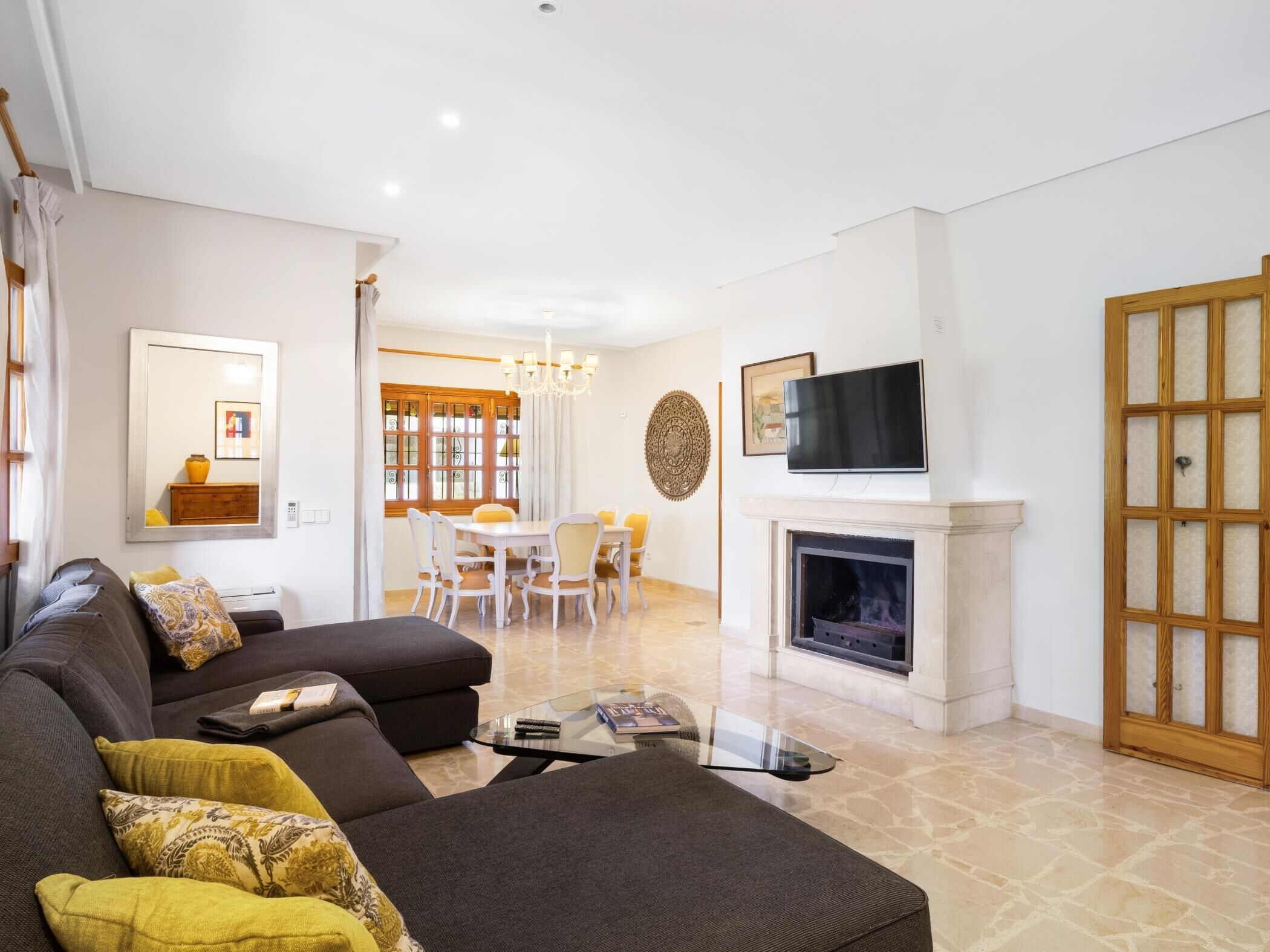 A modern living room with a sofa, a glass coffee table, a fireplace, and a dining area with a chandelier.