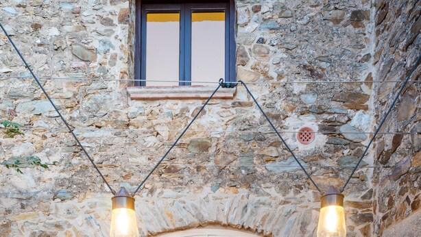 A stone building with a wooden deck, a glass door leading to a kitchen area, and two hanging light fixtures. - Holiday rental townhouse with swimming pool in Begur, Centre (Begur)