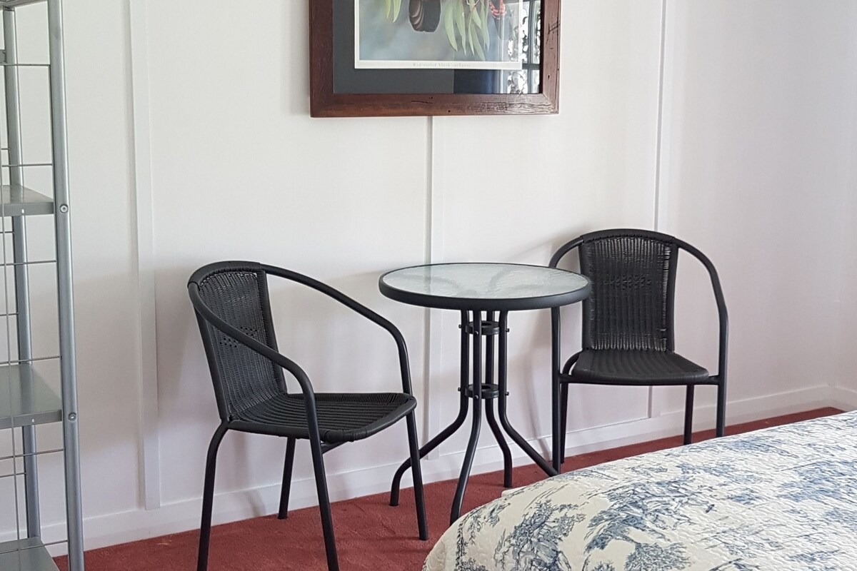 Ein Hotelzimmer mit einem Bett, zwei Stühlen, einem kleinen Tisch und einem Bilderrahmen mit Vogelmotiven an der Wand.