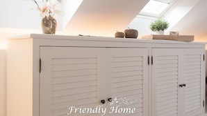 A white cabinet with louvered doors, a vase with flowers, and a small plant on top. - Friendly Home - "Helles Dachstudio" - Cologne - Fair - Bonn - Phantasialand (Bornheim)