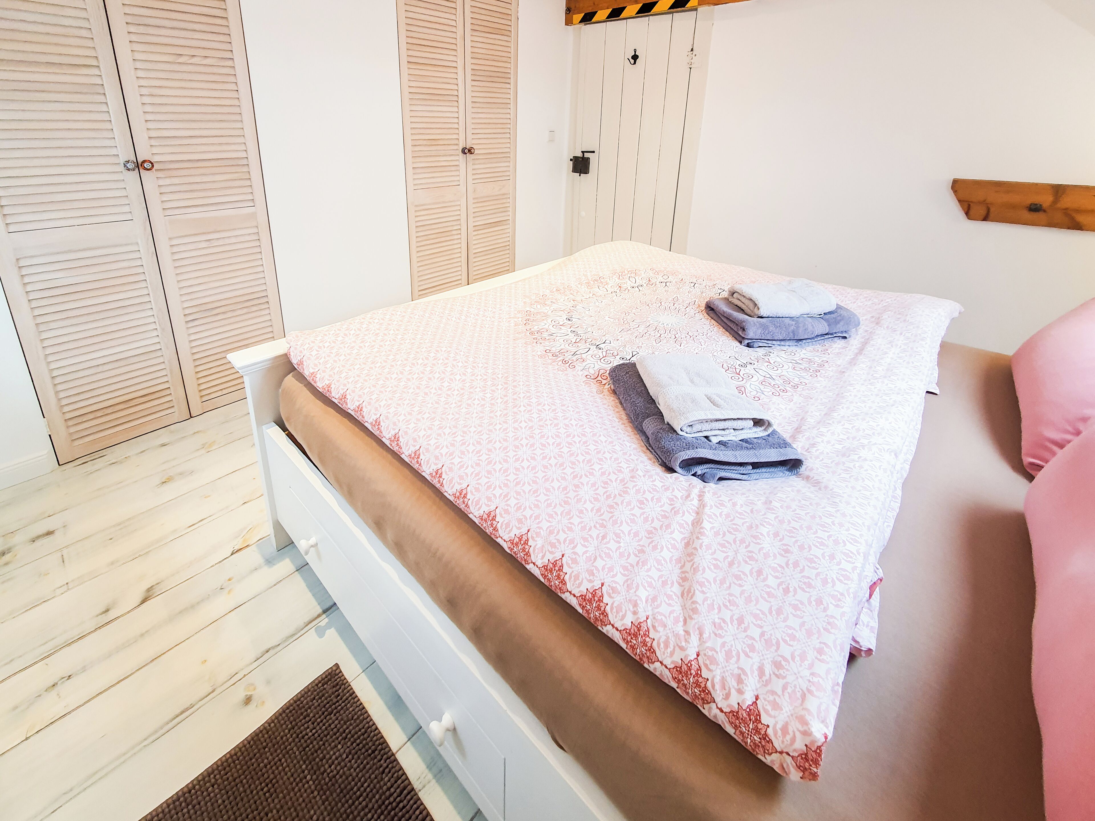 A bedroom with a bed, a wooden floor, a white wardrobe, and a wooden shelf.