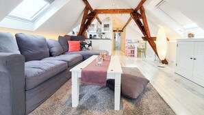 A loft-style living room with a grey sofa, a white coffee table, and a dining area with a pink chair. - Friendly Home - "Helles Dachstudio" - Cologne - Fair - Bonn - Phantasialand (Bornheim)