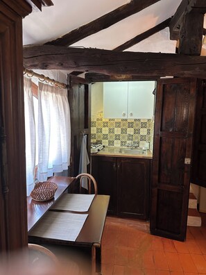 Une cuisine rustique avec des poutres en bois, un mur recouvert de carreaux et une fenêtre agrémentée de rideaux.