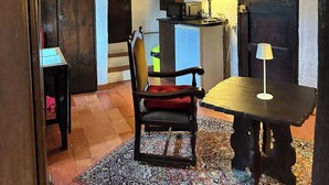Un intérieur rustique avec des poutres apparentes, une table à manger avec une chaise, un petit coin cuisine et un tapis à motifs.